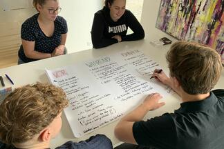 Vier Azubis sitzen mit einem Plakat am Tisch